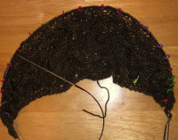 a crescent shape of knitting, a dark brown cresent against blond wood, at least 6 inches at the widest