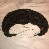 a crescent shape of knitting, a dark brown cresent against muslin fabric, eyelets visible at long end